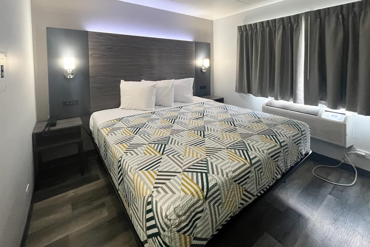 A modern hotel room with a large bed, a headboard with integrated lighting, a built-in heater, and a window with curtains.
