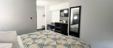 A modern hotel room with a large bed, a desk, a chair, and a mirror.