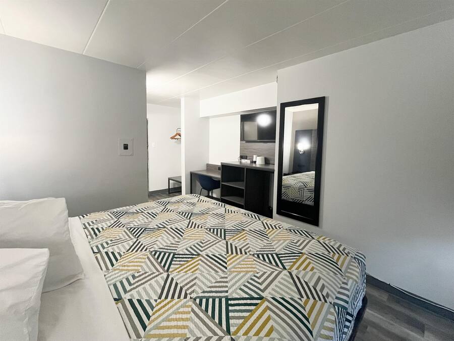 A modern hotel room with a large bed, a desk, a chair, and a mirror.