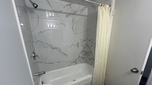 A bathroom with a marble wall, a bathtub, a toilet, and a shower curtain. - Motel 6 - Chicago, IL (Chicago)