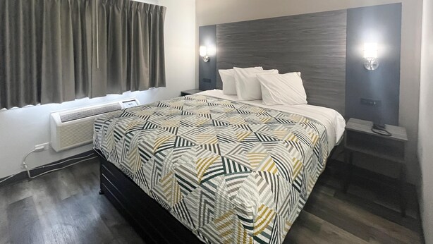 A modern hotel room with a large bed, a bedside table, a nightstand, and a wall-mounted light fixture. - Motel 6 - Chicago, IL (Chicago)