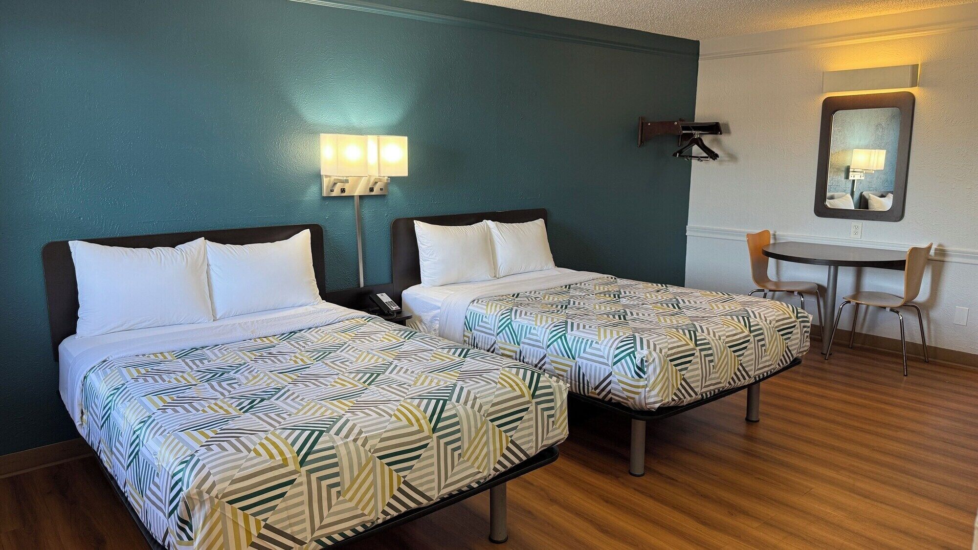 Two single beds with patterned bedding, a desk with a chair, and a wall-mounted lamp.