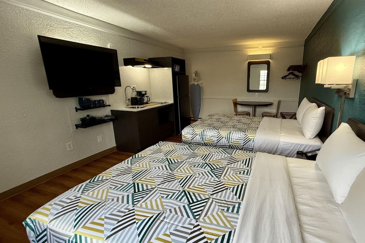 Ett hotellrum med två sängar, ett litet pentry, en tv, en spegel och ett litet bord.