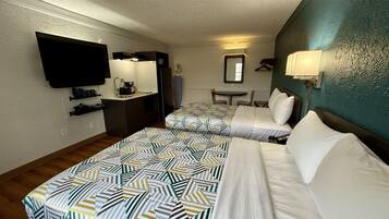 A hotel room with two beds, a kitchenette, a television, a mirror, and a small table.