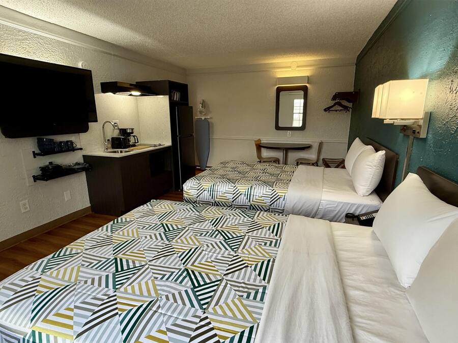 A hotel room with two beds, a kitchenette, a television, a mirror, and a small table.