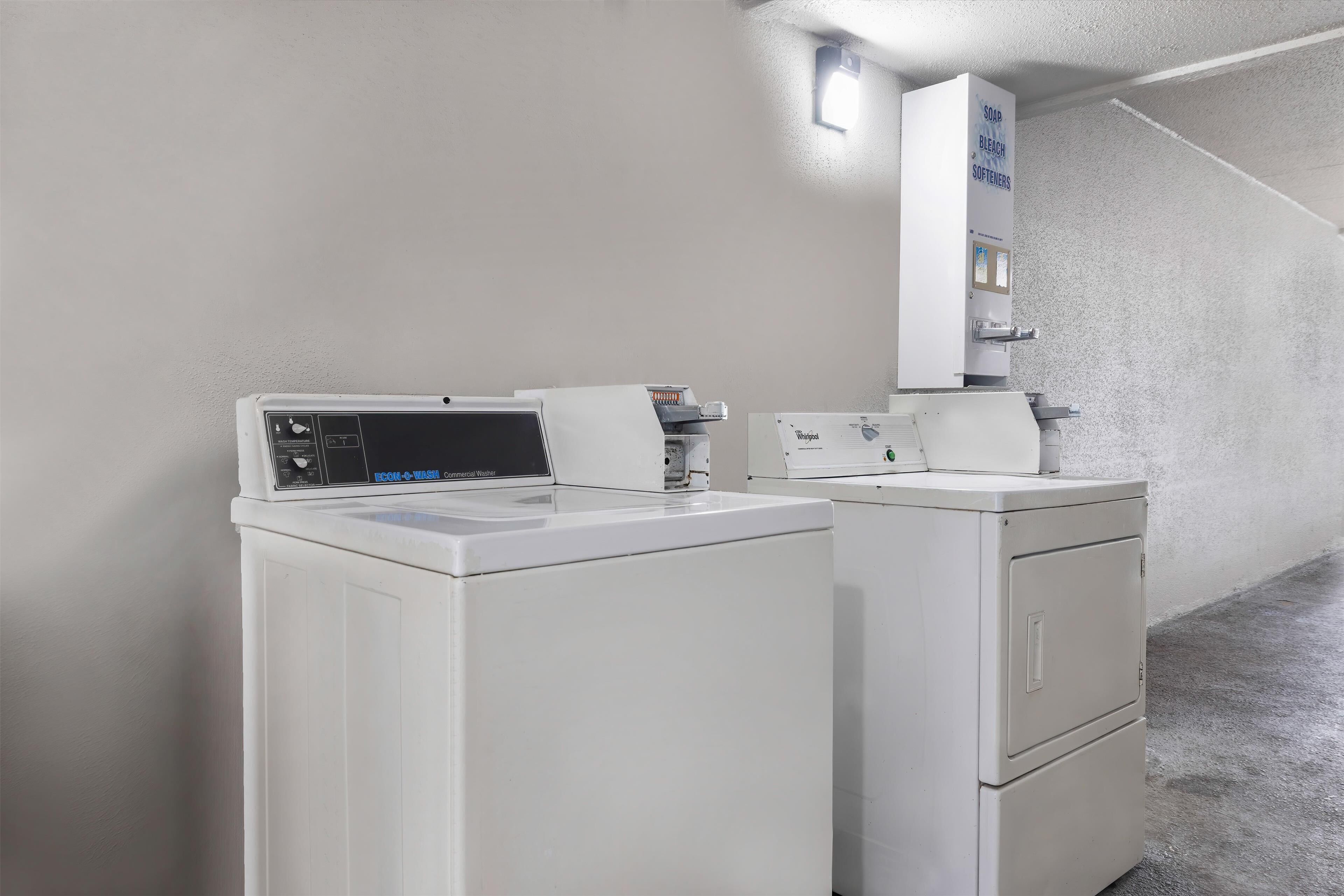 Un'area lavanderia con lavatrice e asciugatrice a carica frontale, un distributore per ammorbidente, sapone e candeggina, e un elettrodomestico Whirlpool.