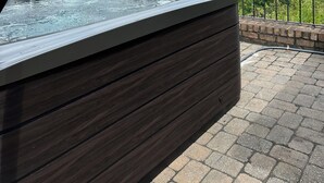 A hot tub with a wooden bench, surrounded by a brick wall and metal railing, overlooking a mountainous landscape.