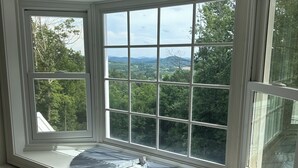A bay window with multiple panes, a white window sill, and a view of a green landscape with trees and hills.