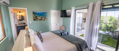 A bedroom with a bed, bedside lamps, a TV, a painting, and a view of the outdoors.