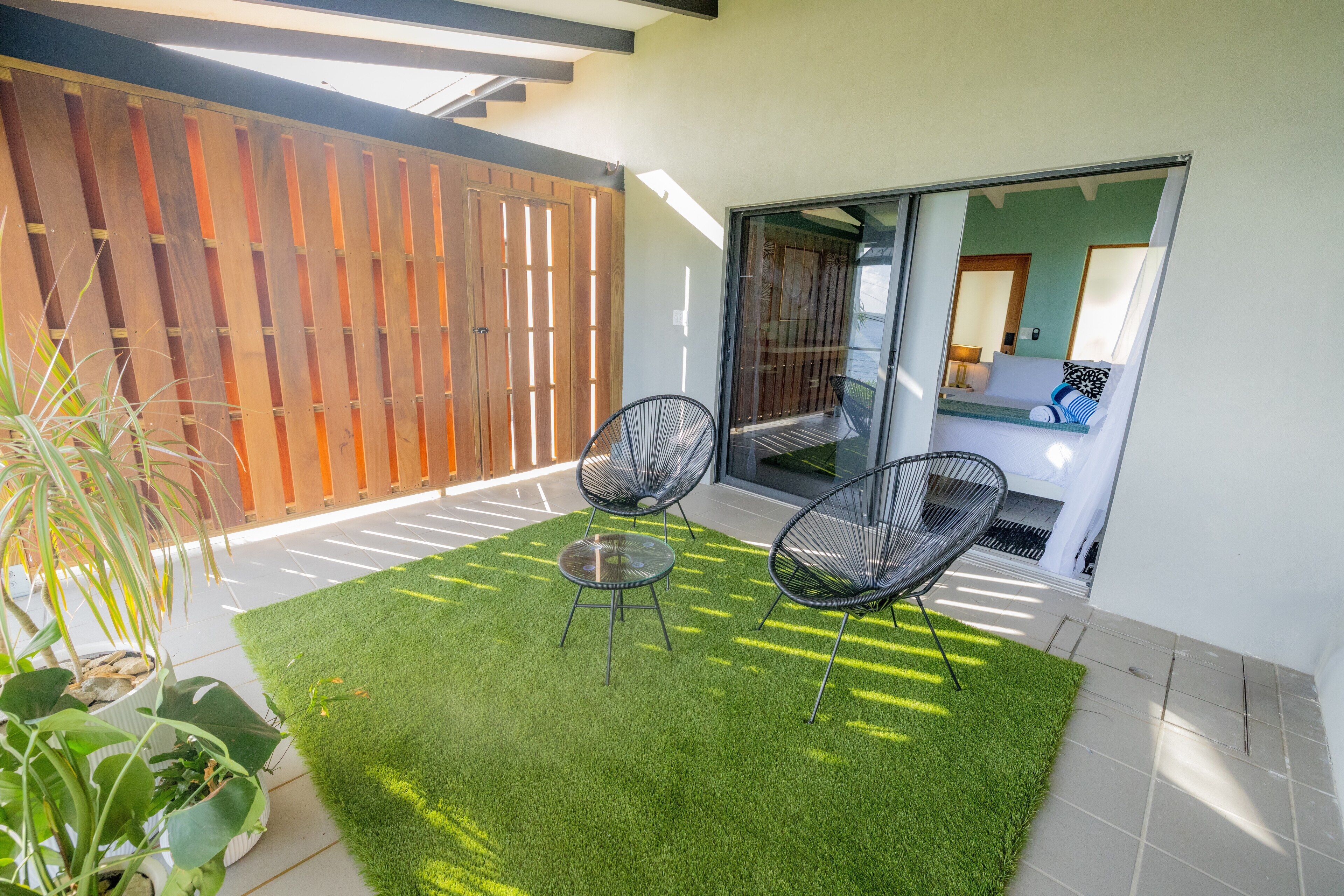 Une terrasse avec du gazon synthétique, deux chaises noires et une plante en pot.