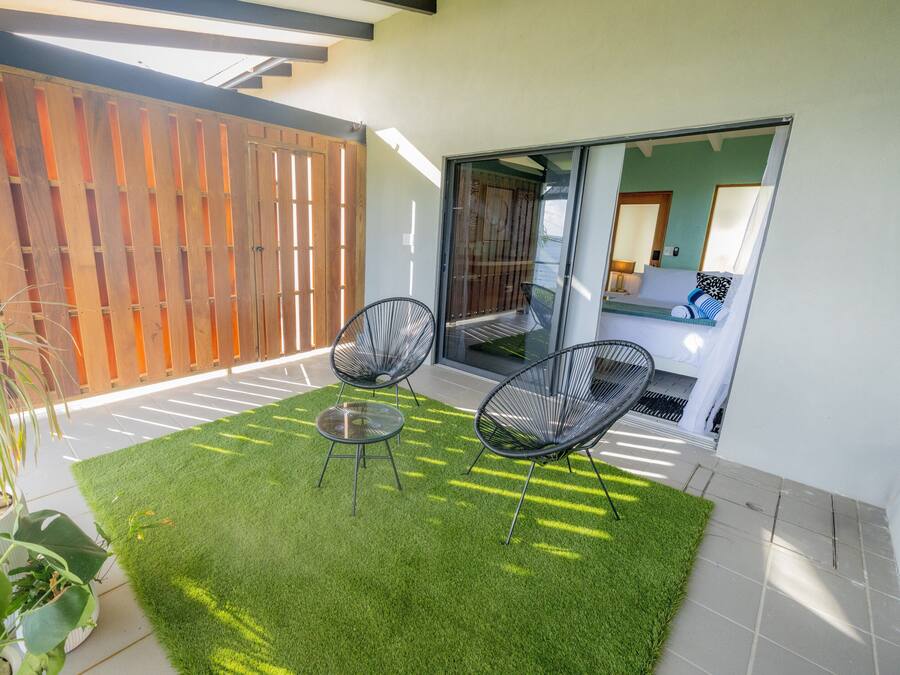 A patio with artificial grass, two black chairs, and a potted plant.