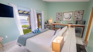 A bedroom with a bed, bedside table, lamp, desk, chair, and artwork on the wall. - The Saint Resort (St. John)