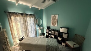 A bedroom with a bed, a chair, a desk with a computer, a mirror, and a wall-mounted decorative piece. - The Saint Resort (St. John)