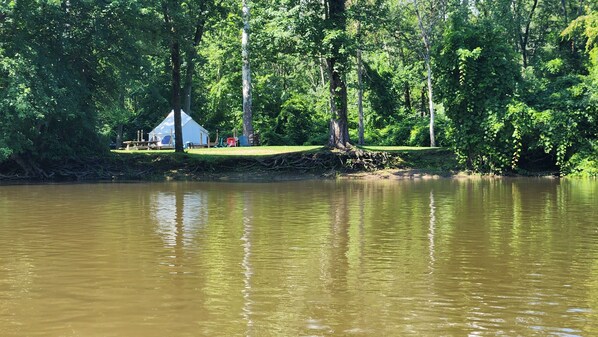 A tented campsite by a calm lake surrounded by dense trees.