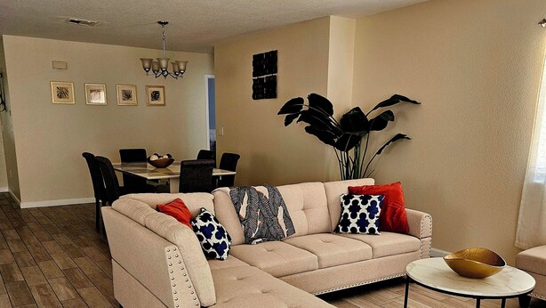 Ein Wohnzimmer mit einem beigefarbenen Ecksofa, einem runden Couchtisch und einem Essbereich im Hintergrund.