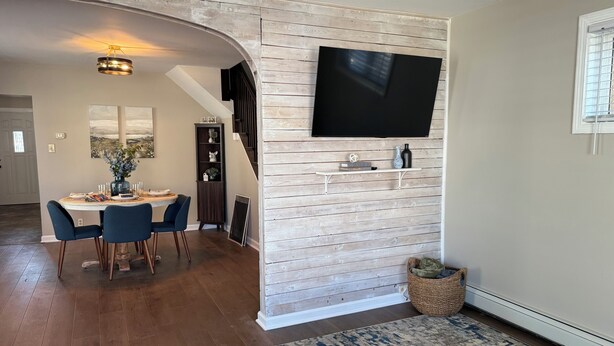A dining area with a wooden wall, a mounted TV, and a staircase leading to another level. - The Blue Jay - Cozy 1-bedroom house in Virginia with WiFi, sleeps 4 (Virginia)