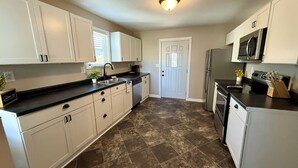 A kitchen with white cabinets, a black countertop, a stainless steel refrigerator, and a microwave. - The Blue Jay - Cozy 1-bedroom house in Virginia with WiFi, sleeps 4 (Virginia)