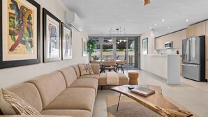 Ein modernes Wohnzimmer mit Sofa, Couchtisch und Essbereich. Es gibt eine Küche mit Kühlschrank und Mikrowelle.