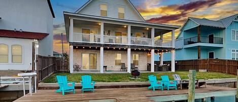 A waterfront property with a dock, outdoor seating, and a large house with multiple balconies.