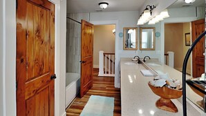 Un bagno con porte in legno, una vasca, un mobile lavabo con due lavandini e uno specchio.