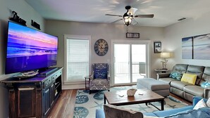 Un soggiorno con televisione, ventilatore a soffitto, divano, tavolino e tappeto decorato.