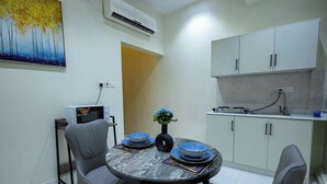 A compact kitchen with white cabinets, a microwave, and a sink. A dining table with blue plates and a vase of flowers is set in the center. - Centrally Located Self Checkin Luxury  Apartment (Riyadh)