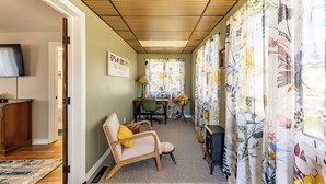 A hallway with a wooden ceiling, a television, a desk with a chair, and floral curtains.