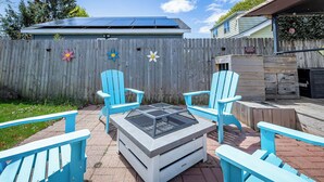 A backyard with a fire pit, four blue Adirondack chairs, and a wooden fence with flower decorations.