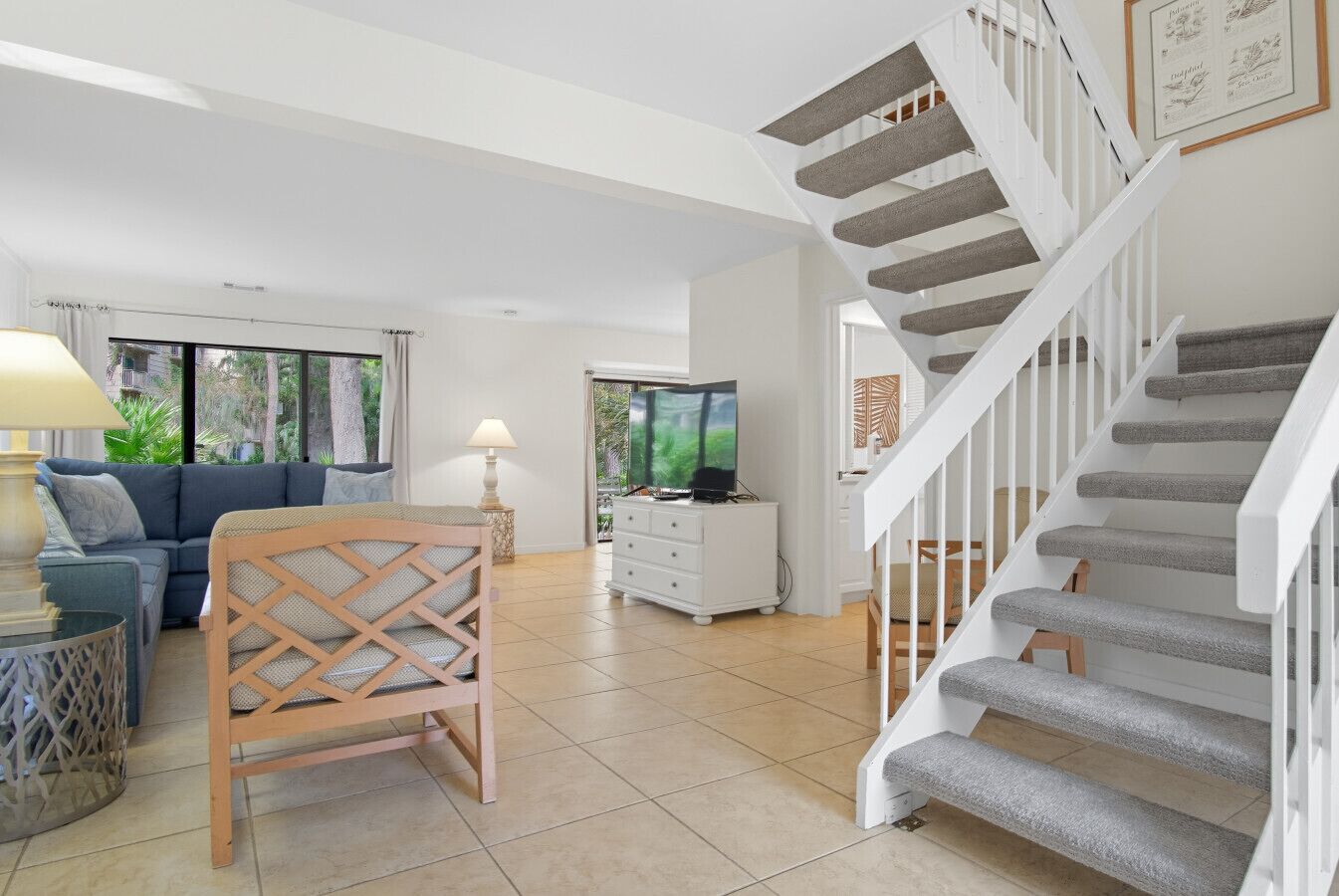 A spacious living room with a wooden chair, a sofa, a TV, and a staircase with grey carpeted steps.