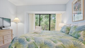 Une chambre avec un lit, une télévision, une lampe et un balcon donnant sur des palmiers.