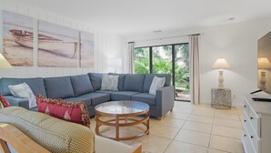 Un salon moderne avec un canapé d’angle gris, une table basse ronde et une grande fenêtre avec des rideaux.