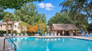 Une piscine dotée de chaises longues et d’un espace abrité, entourée d’arbres et de bâtiments.