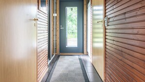 Un couloir aux murs lambrissés, une porte sombre et un sol carrelé.