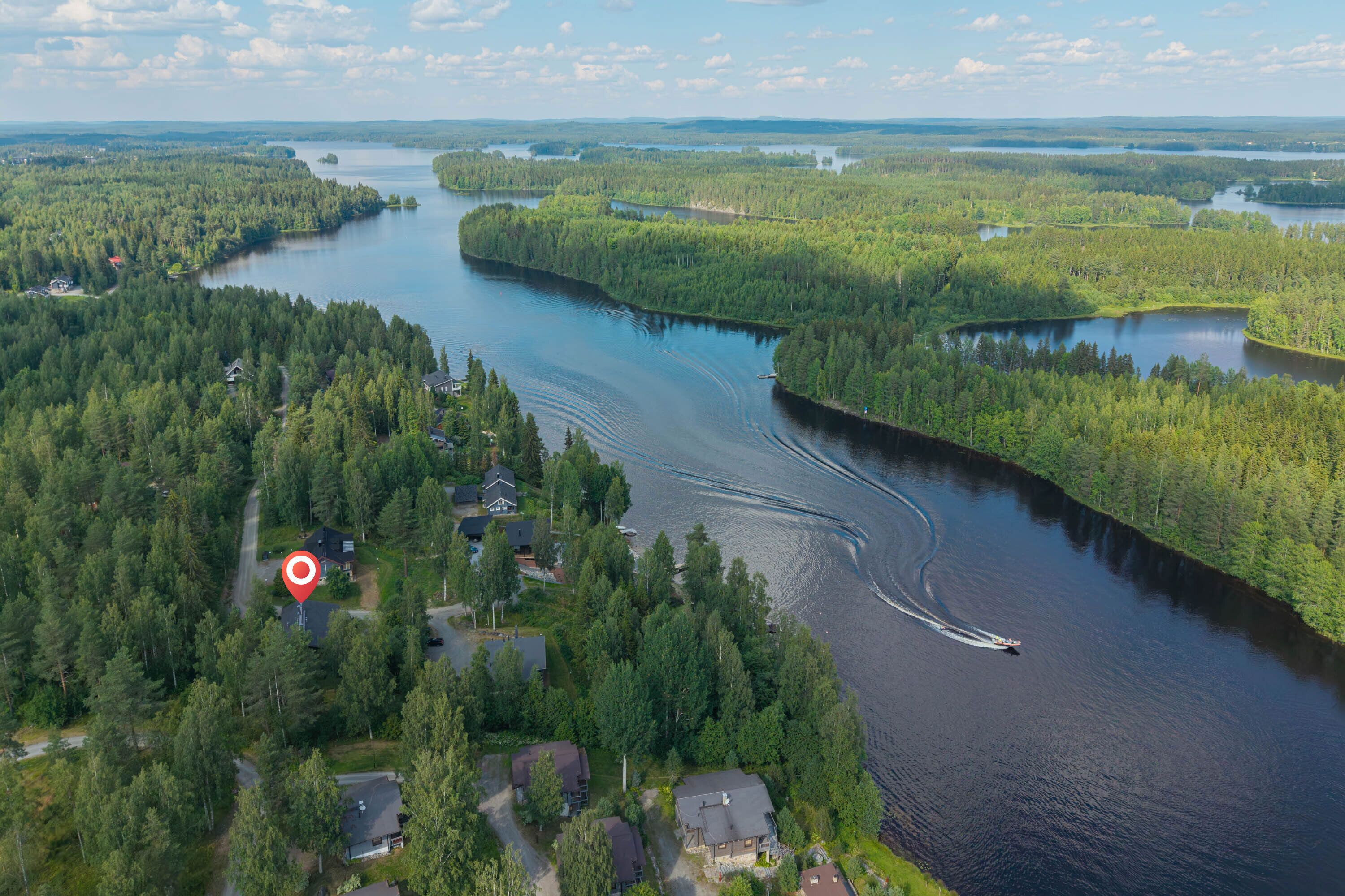 An aerial view of a river surrounded by dense forests, with a house marked by a red pin on the left.