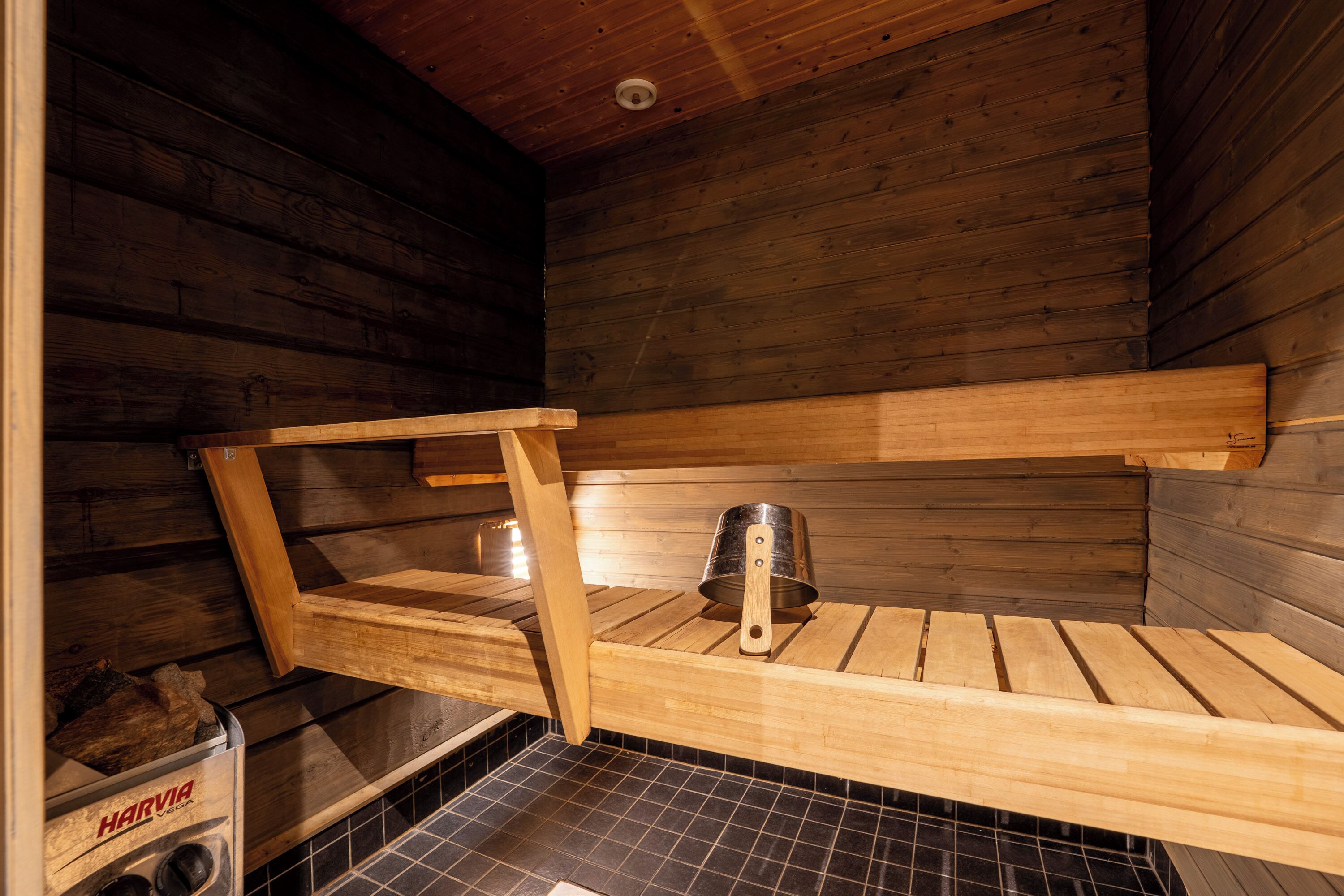 A sauna with wooden benches and a metal bucket.