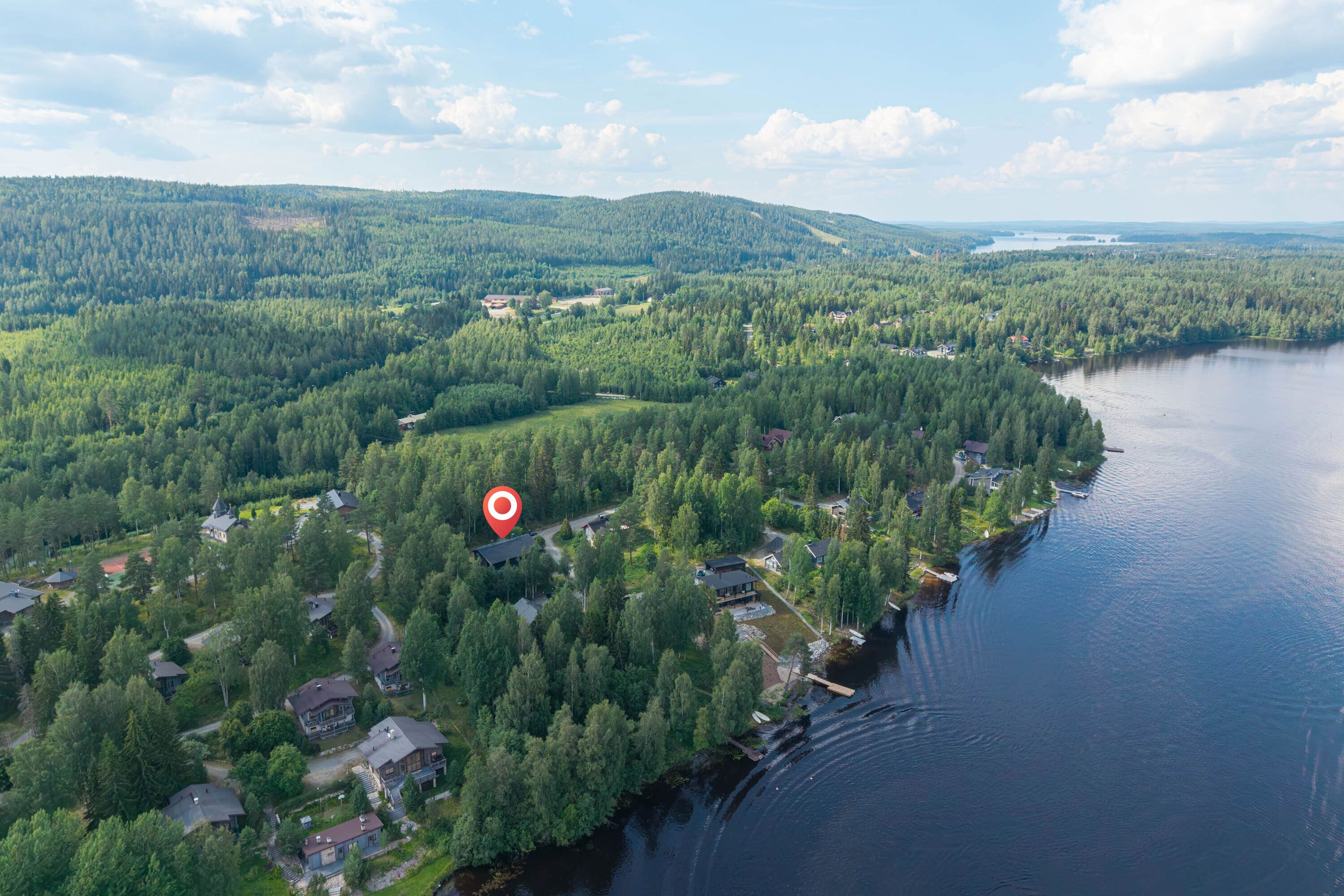 An aerial view of a lakeside residential area with houses surrounded by dense forests and a large body of water.