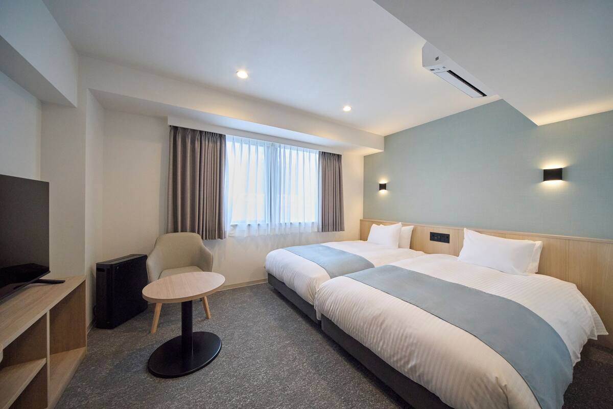 A hotel room with a large bed, a desk, a chair, a small table, and a television.