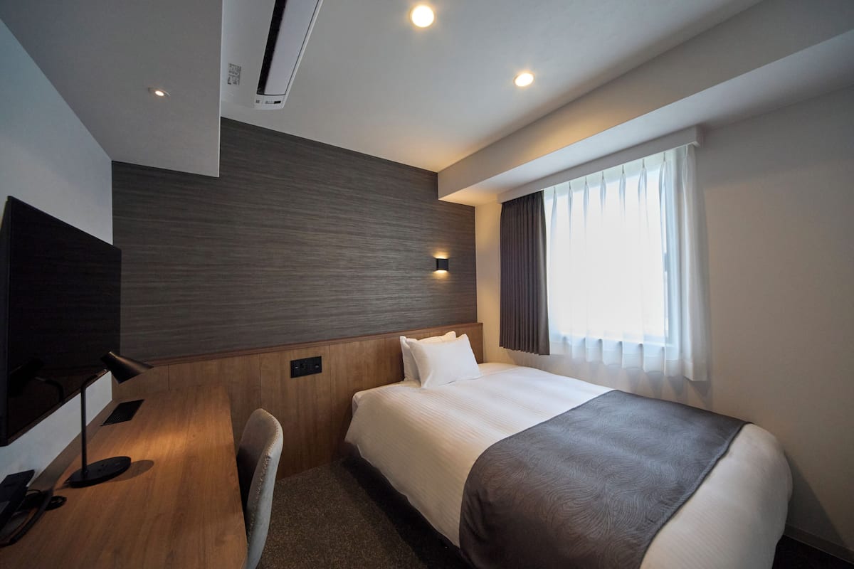 A modern hotel room with a large bed, a desk, and a TV.