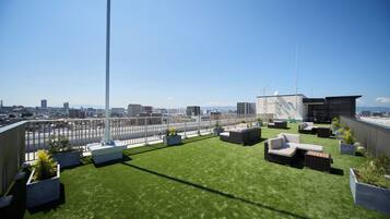 A rooftop terrace with artificial grass, outdoor seating, and city views.