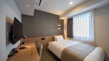 Quarto de hotel com cama, escrivaninha, cadeira, televisão de tela plana e janela com cortinas.