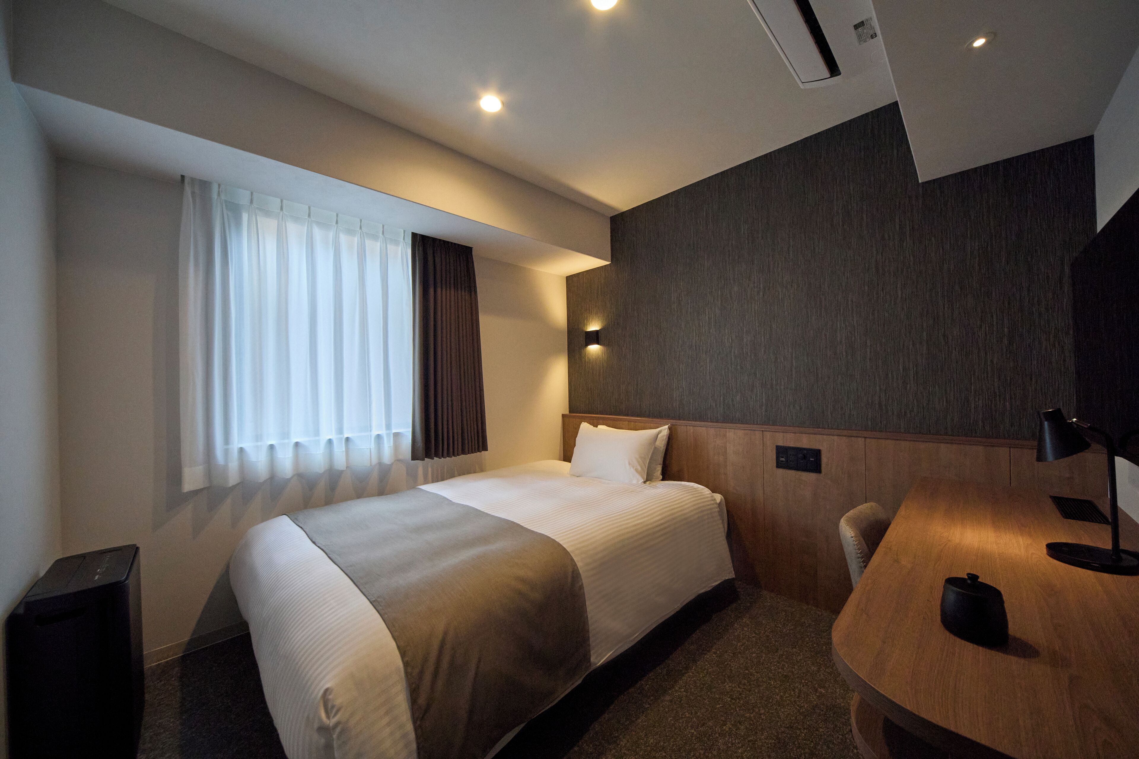 A hotel room with a large bed, a desk, a chair, a lamp, and a small table.