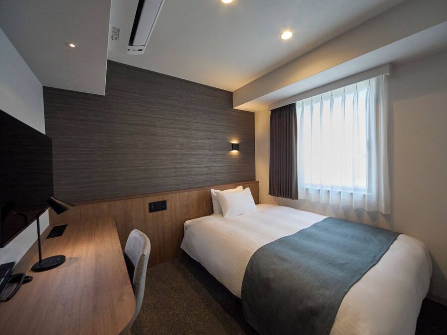 A hotel room with a bed, a desk with a telephone, a television, and a window with curtains.