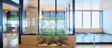 A modern indoor space with a glass partition, a water feature, and a seating area with chairs.