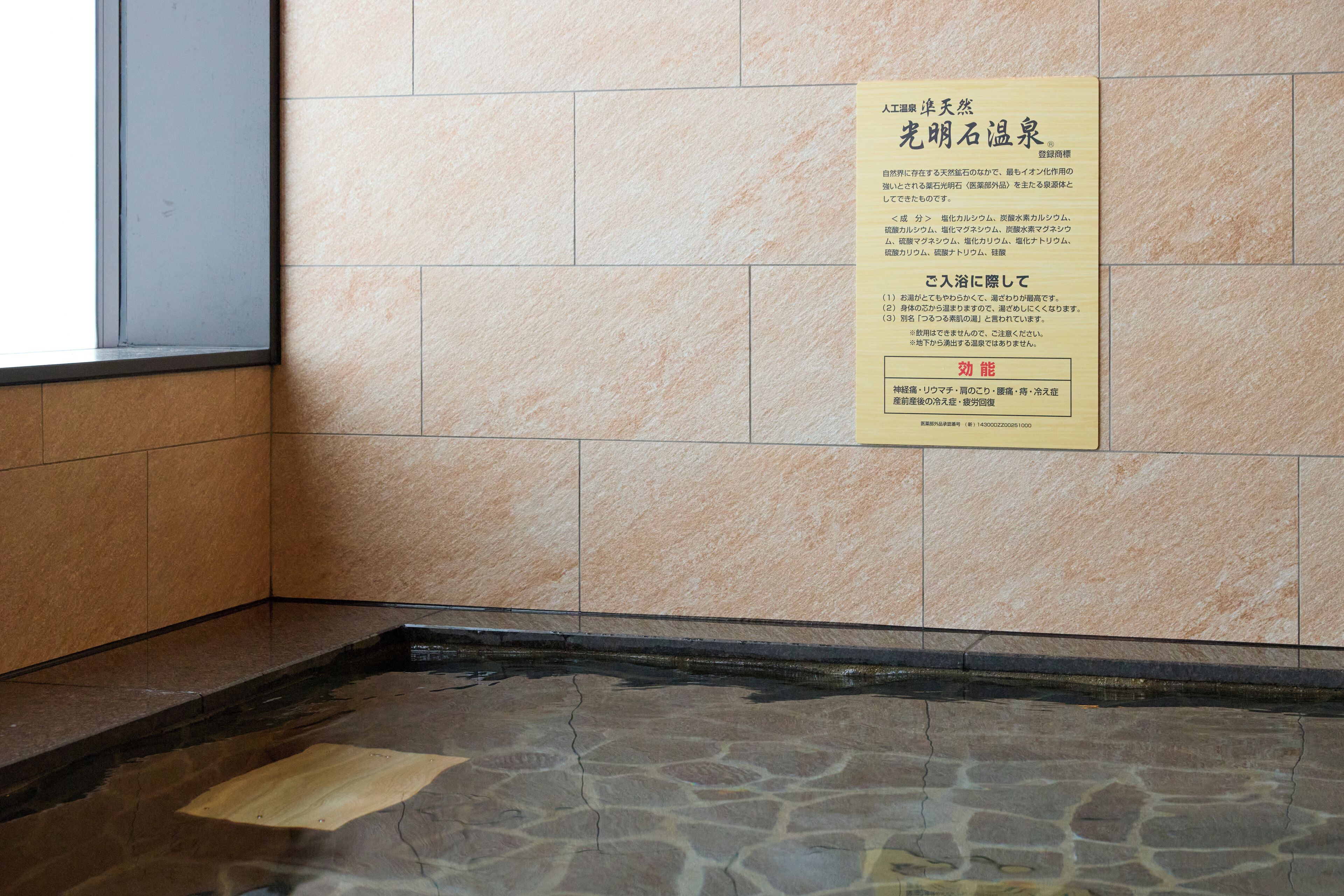 Een betegelde muur met een bord in Japanse tekst, een stenen vloer en een raam aan de linkerkant.