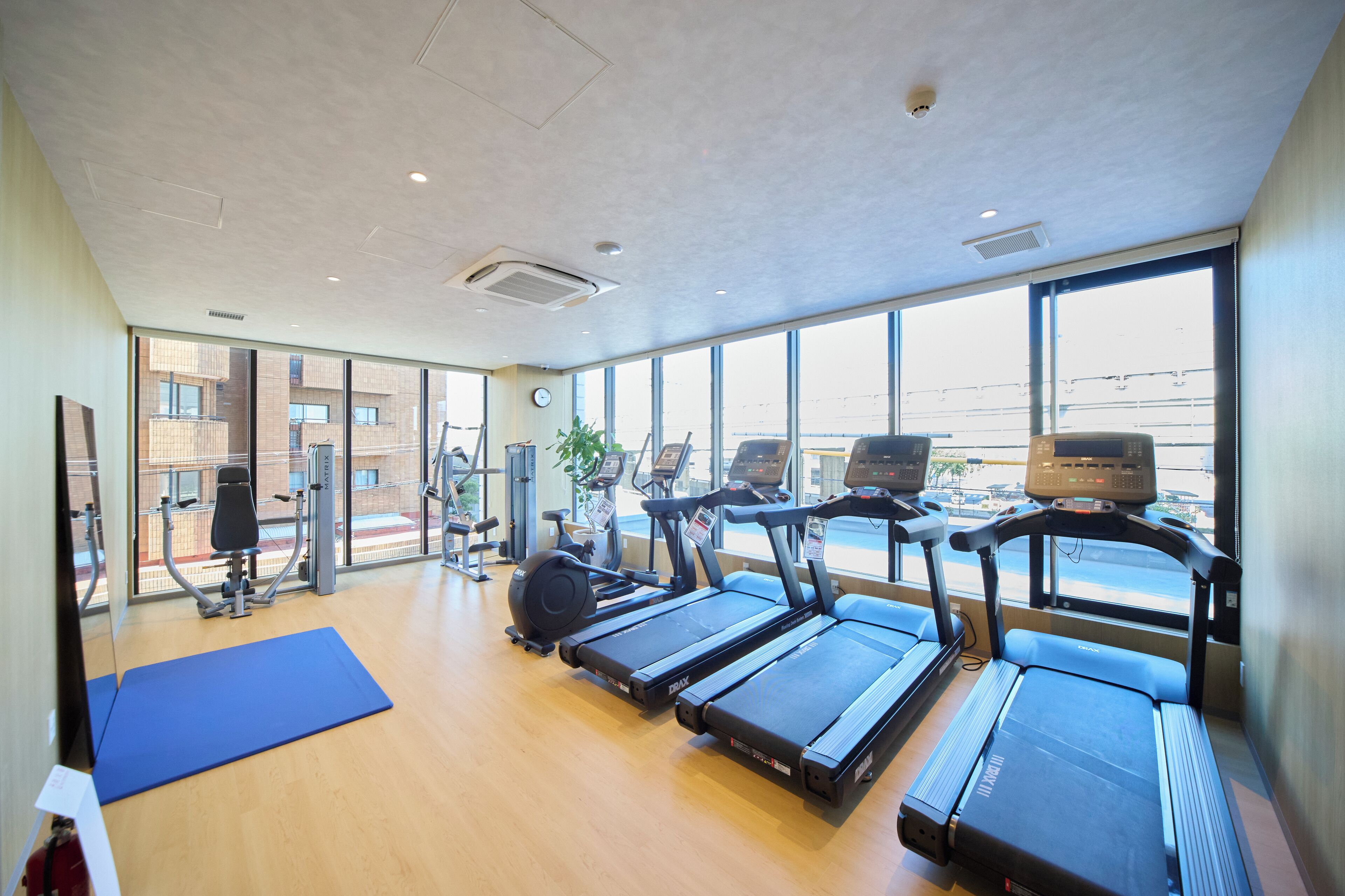 Un gimnasio con cintas de correr, máquinas de ejercicio y ventanas amplias.