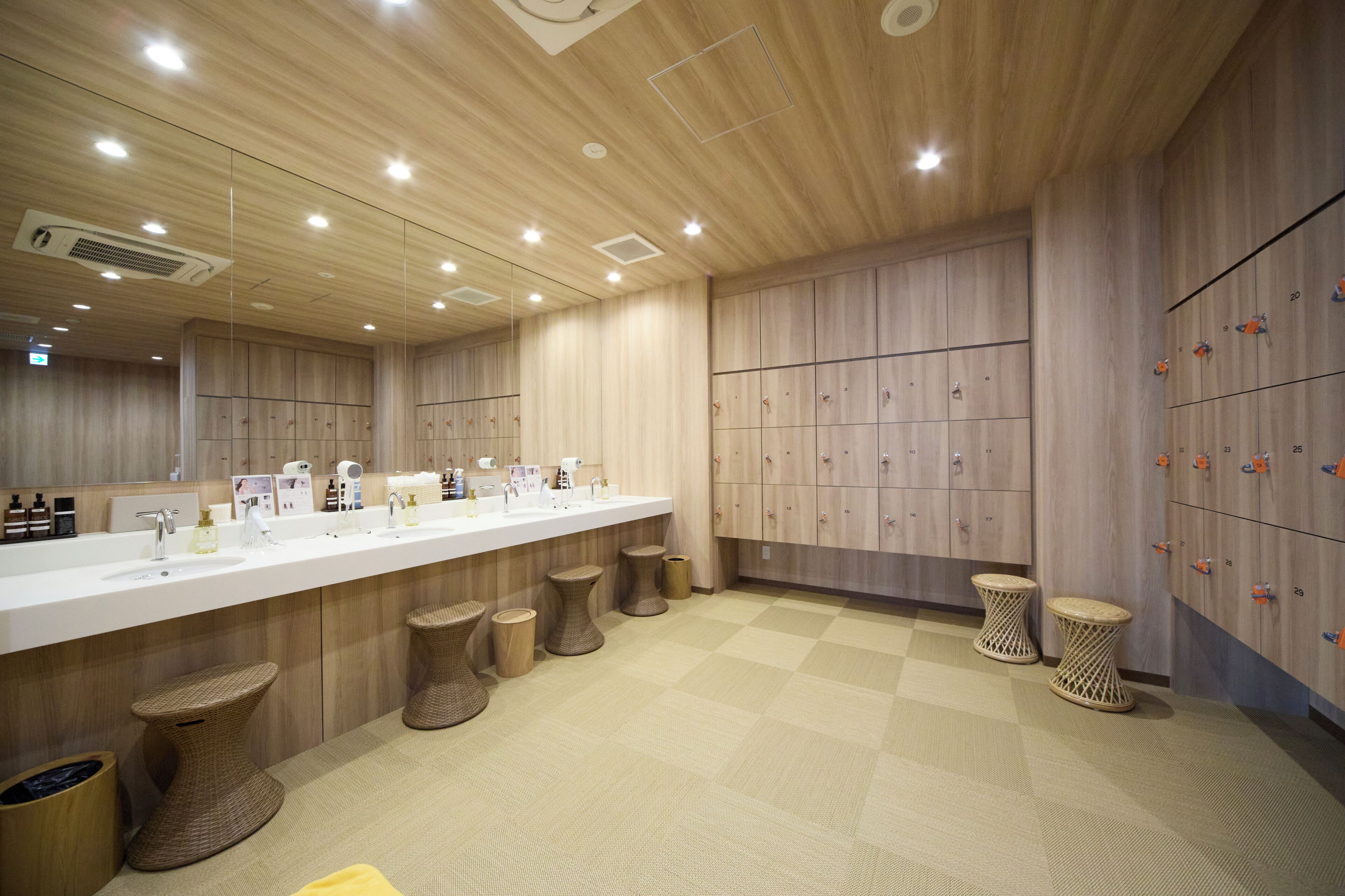 A modern bathroom with a wooden vanity, multiple sinks, and a locker area.