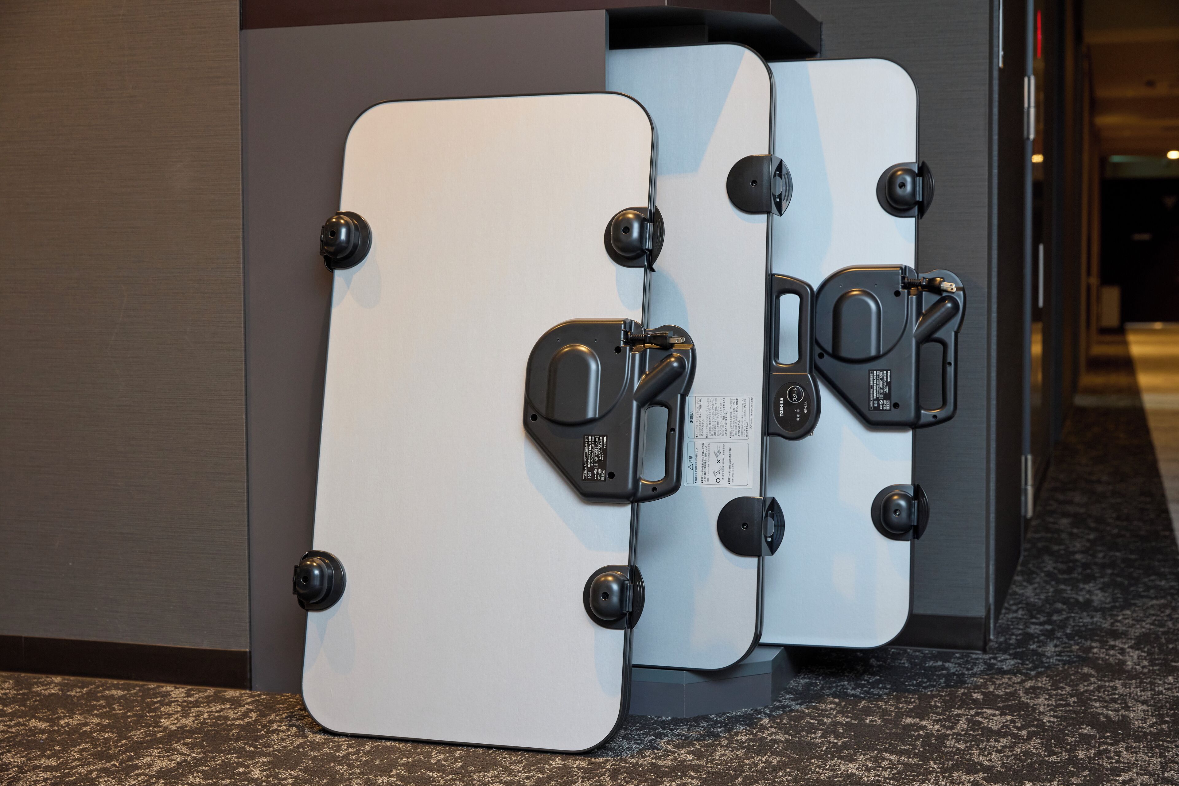 Three white suitcases with black clasps and wheels, leaning against a wall in a hallway.