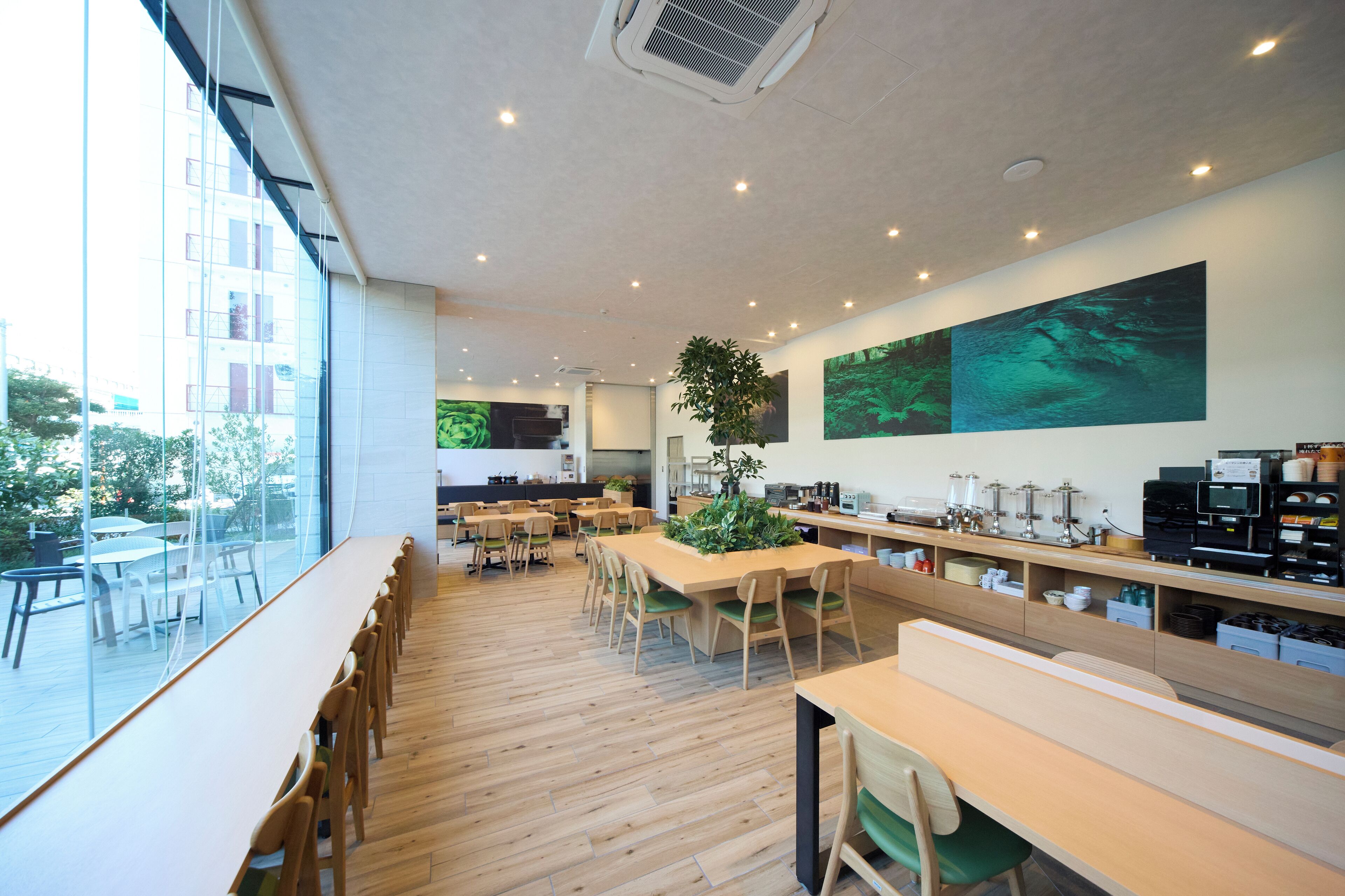 A modern dining area with wooden tables and chairs, large windows, and artwork on the walls.