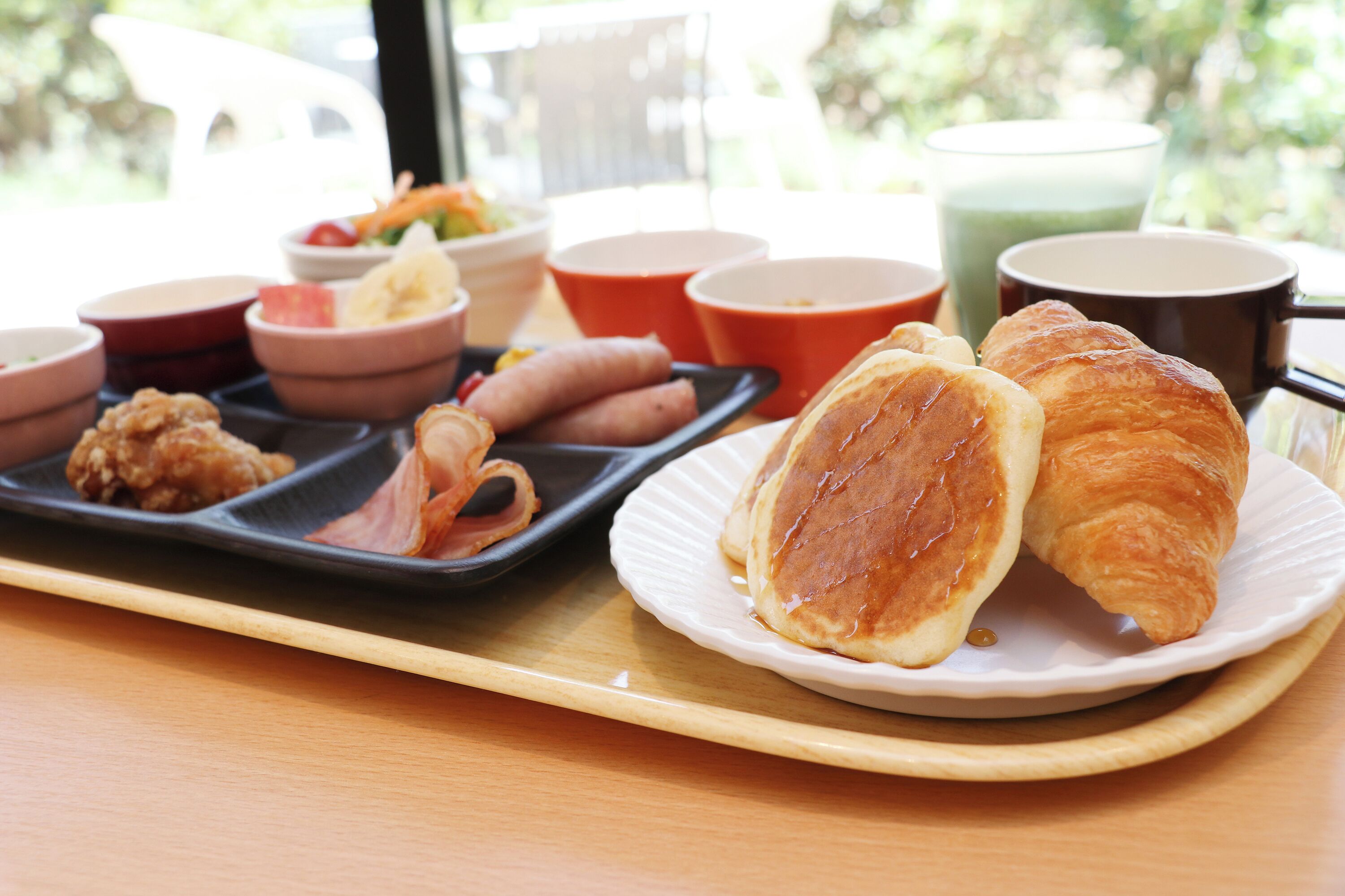 A breakfast tray with croissants, pancakes, and a variety of side dishes.