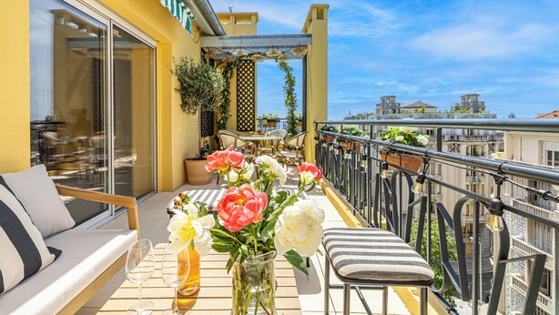 A balcony with a sofa, a dining table with chairs, and a vase of flowers. - Exceptional Penthouse, 2 BDR Suites, 3 spacious terraces, Sea view, Elevator, AC (Nice)